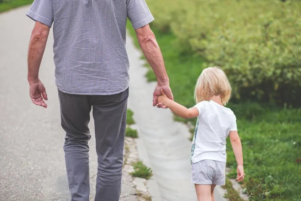 Avô e neta caminhando de mãos dadas por uma trilha